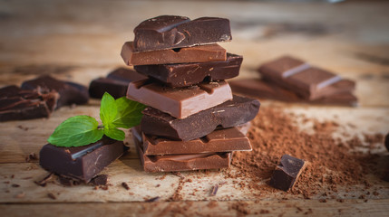 Close-up of stacked dark and milk chocolate with fresh mint on wooden background  - obrazy, fototapety, plakaty