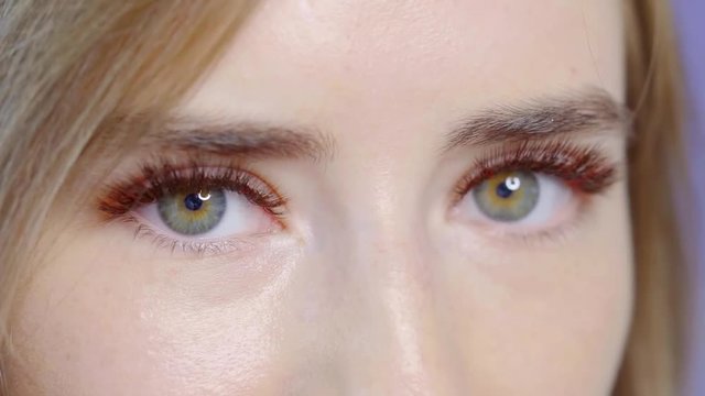 close-up of beautiful green eyes of young woman, she is blinking and demonstrating her extended false lashes