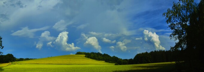 Naklejka na ściany i meble Scenic landscape with storm cloud in background over green agriculture fields,trees and meadows at spring daylight, dramatic clouds, sky.Relaxing nature,sunshine.Panoramic photo.Czech Repulic, Europe.