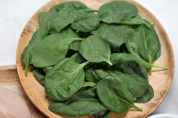 Leaves of fresh spinach on a round wooden plate. Light background. Close-up. View from above.