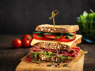 Rolgordijnen Close-up of delicious Sandwich with salami, cheese and fresh vegetables on rustic wooden cutting board on wooden table, selective focus. Space for text. Horizontal. Club sandwich concept. © Mila Bond