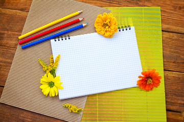 Blank spiral notepad with yellow and orange flowers, colorful pencils and corrugated cardboard...
