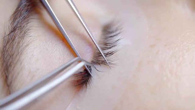 beautician is correcting false lashes and separating filament on female eyelids, close-up in beauty salon