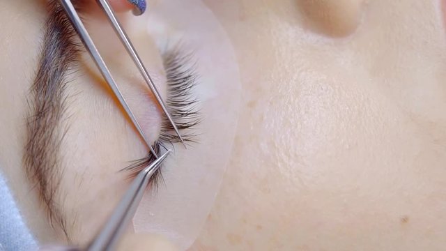 master is performing procedure of lash extension on female eyelids in a beauty clinic