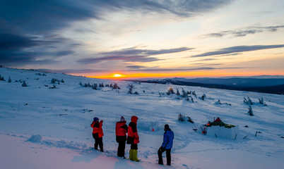 Young people looking to the winter sunset. There is tent and igloo in the background