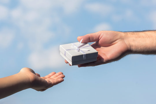Male and female hands with a small white gift boxe on the blue sky background. Concept.