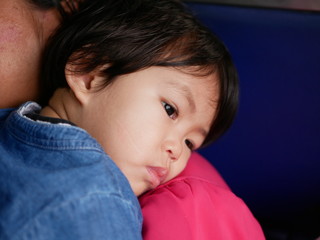 Little Aisan baby girl, 18 months old, leaning on her mother's shoulder - holding baby helps her...