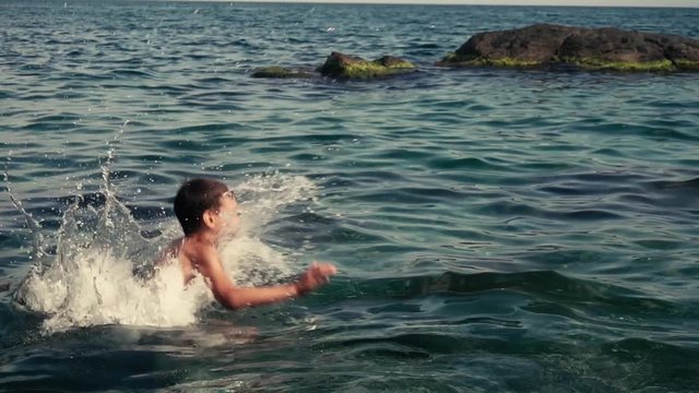 Happy boy is jumping into the sea water during summer holidays. Slow motion.
