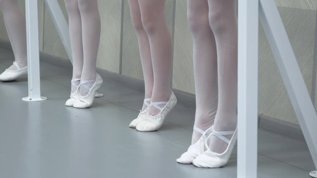 closeup legs of little ballerinas group in white shoes in row practicing in ballet school slow motion. Young girls training elements of classical dance exercise. Childhood, dancing, lifestyle concept