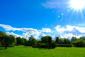 Blue clear sky. The sun's rays over the Park, green grass and trees.