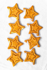 Fototapeta na wymiar Two rows of eight decorative golden stars handmade from dough on a bright white fabric surface