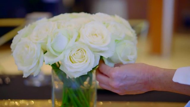 female floral artist is correcting white roses in a vase on table, close-up