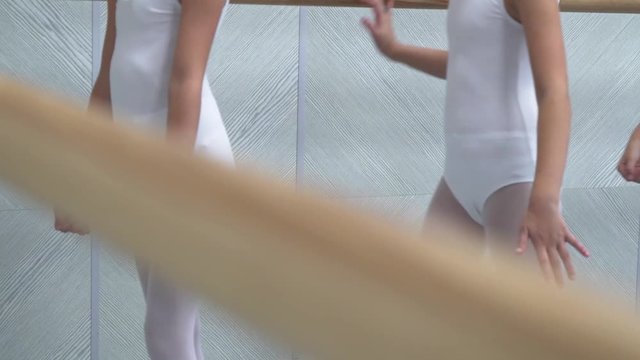 closeup legs of little ballerinas group in white shoes practicing in ballet school, slow motion. Young girls training elements of classical dance exercise. Childhood, dancing, lifestyle concept