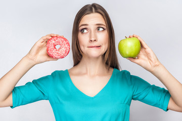 Portrait of dreaming young beautiful girl in blue blouse standing, showing and holding pink donut...
