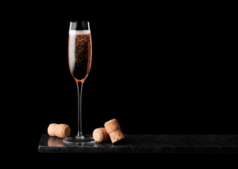 Elegant glass of pink rose champagne with corks on black marble board on black background.