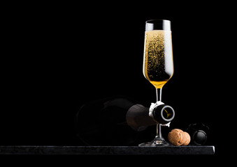 Elegant glass of yellow champagne with cork and wire cage and bottle on black marble board on black background. Space for text © DenisMArt