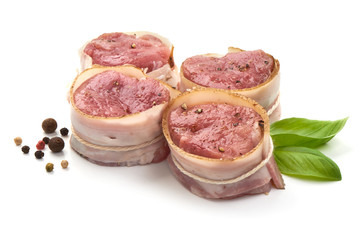 Raw Pork medallions wrapped in bacon with basil leaves and peppercorns, isolated on white background.