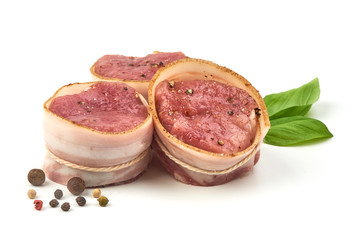 Raw Pork medallions wrapped in bacon with basil leaves and peppercorns, isolated on white background.