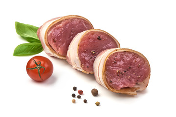 Raw Pork medallions wrapped in bacon with basil leaves and peppercorns, isolated on white background.
