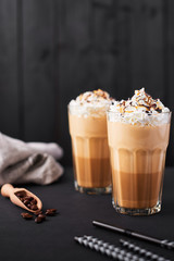 Iced caramel latte coffee in a tall glass with chocolate syrup and whipped cream. Dark wooden background with copy space.