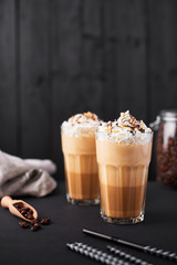 Iced caramel latte coffee in a tall glass with chocolate syrup and whipped cream. Dark wooden background with copy space.