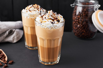 Iced caramel latte coffee in a tall glass with chocolate syrup and whipped cream. Dark background with copy space.
