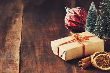 Christmas card with place for your text. Decoration made from a vintage red glass Christmas ball, gift box, sticks with cinnamon and lemon slices, Christmas tree on a brown wooden board