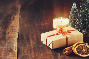 Christmas card with place for your text. Decoration from a box with a gift in kraft paper, sticks with cinnamon and lemon slices, Christmas tree on a brown wooden board