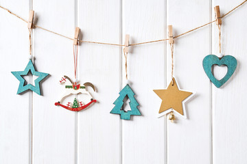 Christmas card with place for your text. Wooden figures of green color in the form of stars, Christmas tree, hearts, horses hanging on clothespins on a rope on a white background of wooden boards
