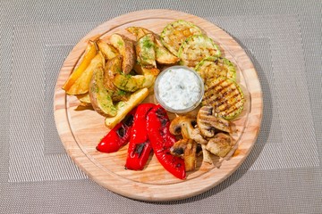 vegetarian grill with zucchini, french fries, mushrooms, paprika, white sauce and dill on wooden plate, flat lay food photo