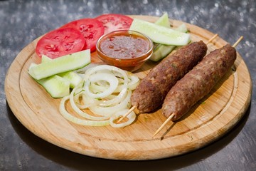 delicious beef cutlet baked and fresh tomatoes and cucumbers, pickled onions, red sauce and dill, served on wooden plate, flat lay food photo