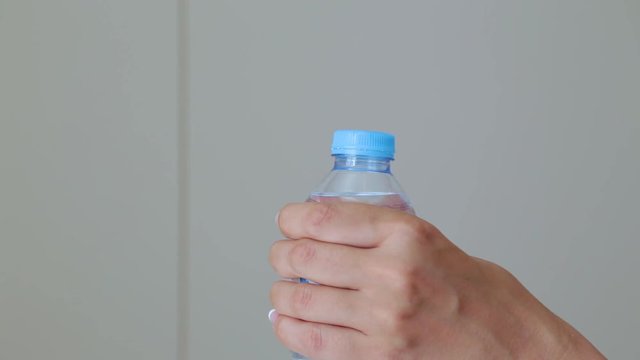 Closeup view of tanned female hands opening closed plastic bottle with fresh clear water isolated at white home interior. Real time full hd video footage.