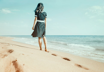 Barefoot woman walking on sand beach leaving footprints.