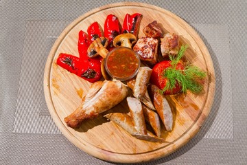 chicken thighs grilled with tomatoes, dill, paprika, served with sausages and mushrooms on wooden plate, tasty flatlay food photo