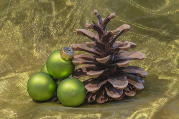 A pine cone and green Christmas tree balls on a colored towel.