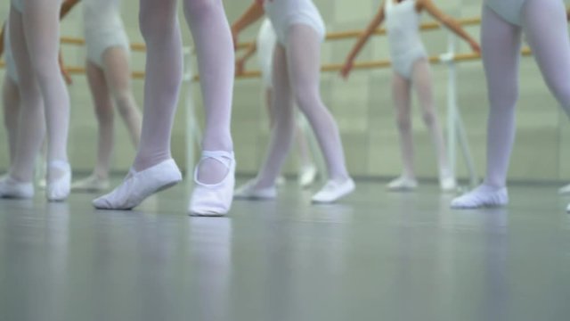 closeup legs of little ballerinas group in white shoes practicing in ballet studio. Young girls training elements of classical dance exercise. Childhood, dancing, lifestyle concept