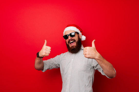 Winter holiday and countdown concept. Man with beard and cheerful face celebrates Christmas. Santa Claus waits for New Year on red background. Santa showing thumbs up