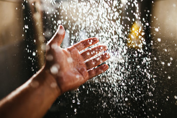 A man's hand in a spray of water in the sunlight against a dark background. Water as a symbol of...