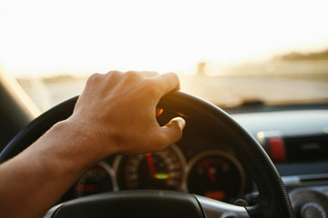 Selective focus man's hand on steering wheel, driving a car at sunset. Travel background