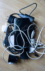 Smartphone tangled in differnt electronics cables chargers usb and black and white wires