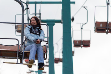 Happy girl in a jacket goes on a chairlift. Peoples