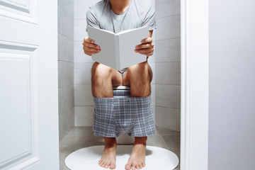 Man sitting on a toilet with a book