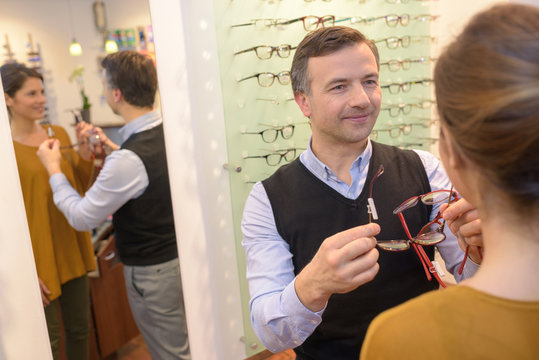 ophthalmologist and beautiful brunette female choosing glasses in optics store