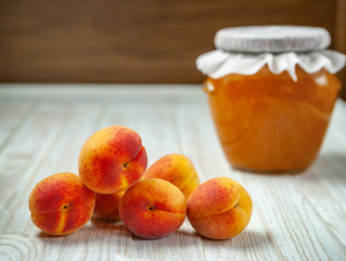 Ripe fresh apricots and apricot jam in a jar on a wooden background. Selective focus, healthy eating
