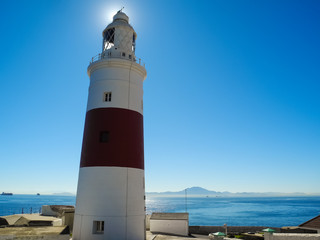 Lighthouse with a sunlight behind on beautiful blue sea and sky background. Gibraltar, Europa point