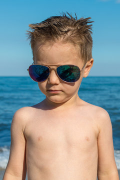 a beautiful little boy posing on a beach by the sea with sunglasses