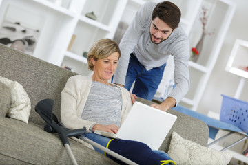 Obraz premium middle-age woman injured sitting on the sofa and using laptop