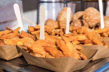 Papaer dishes, coasters with portions of sweet potato chips, batatas. Metal plate with several papaer bowls with sweet potato chips. Asia Street Food Market.