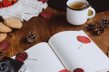  Flat lay view of autumn leaves and tartan textured sweater on wooden background with cup of tea . Autumn or Winter concept.