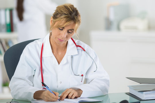 female doctor writing on clipboard at her office